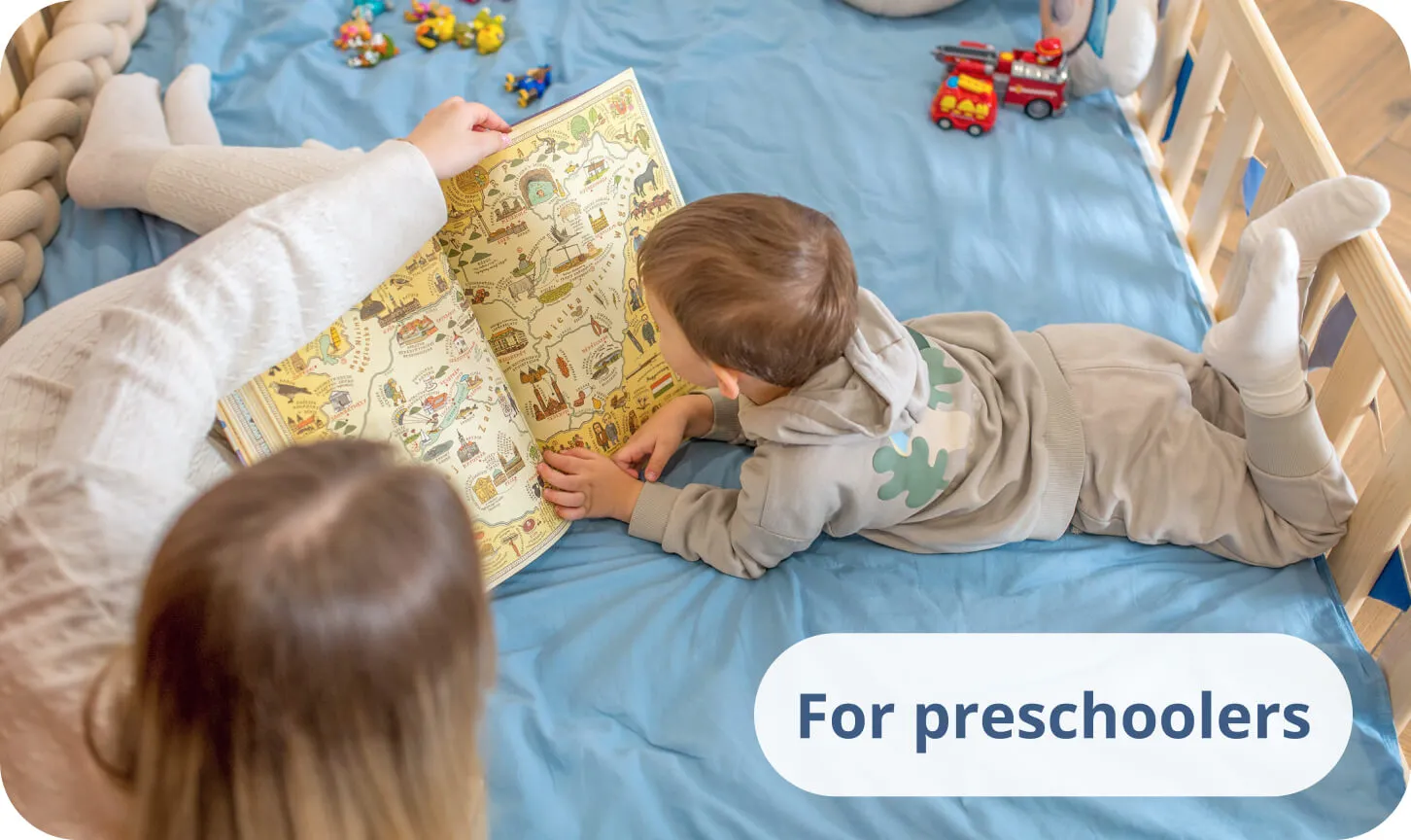 Small boy with his mother reading a colorful book on blue bedding in a pine bed.
